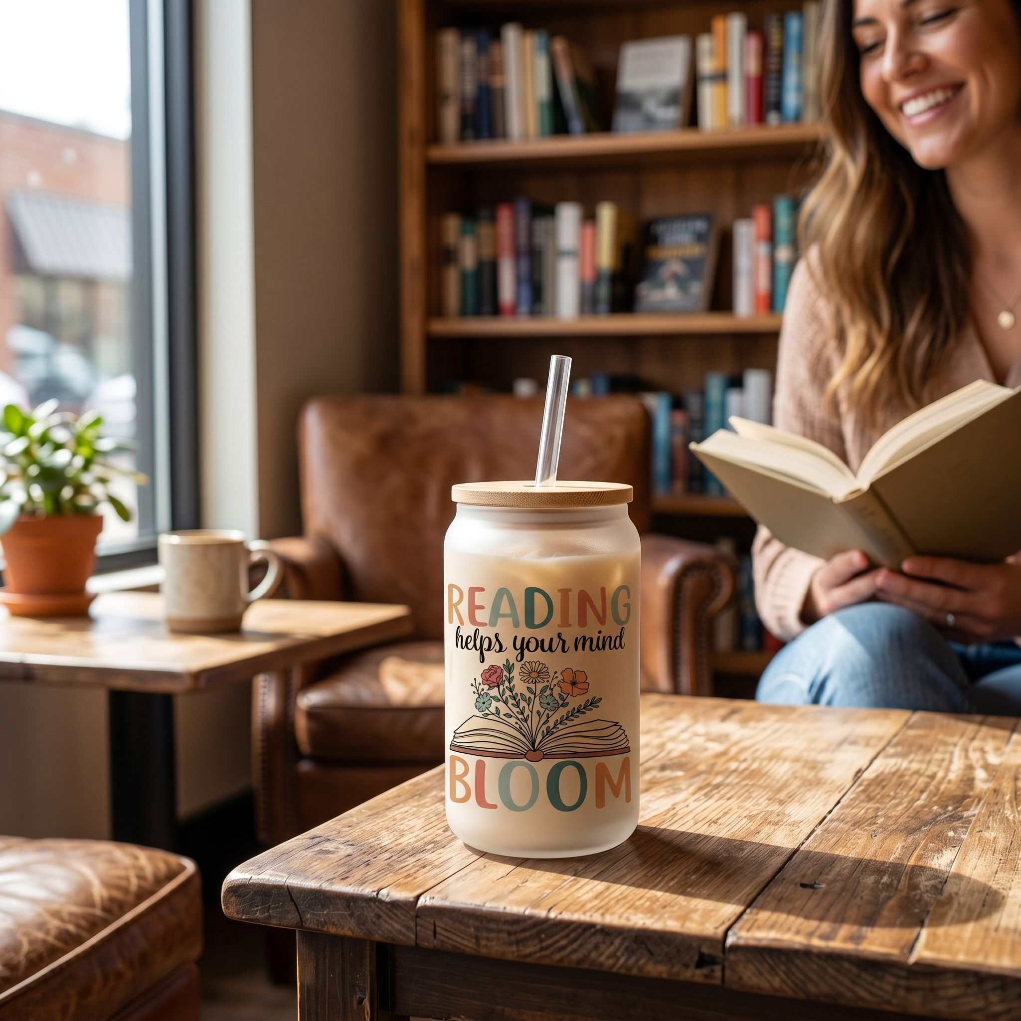 16 oz clear glass Libby cup with book-themed design on rustic wooden table in coffee shop setting
