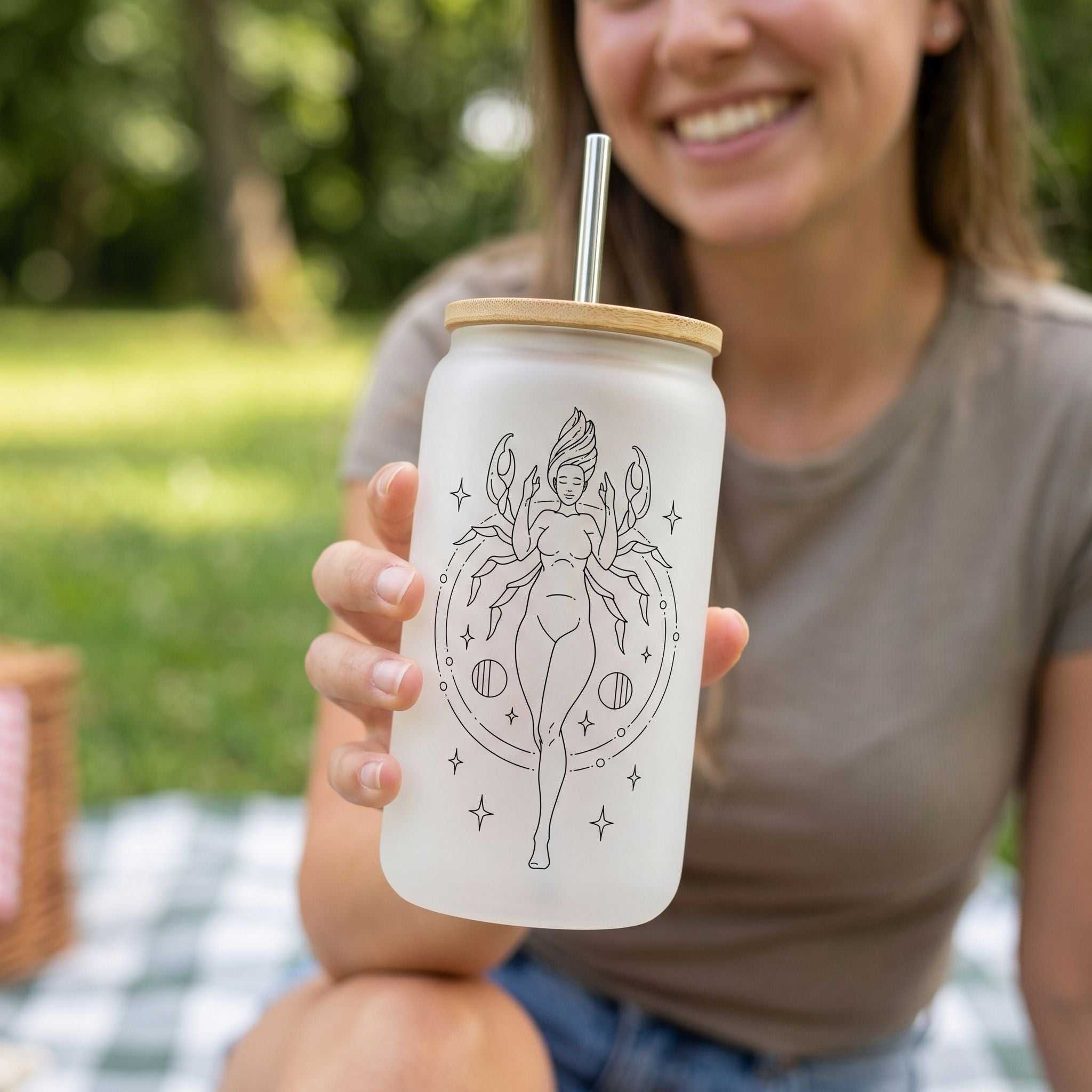 Close-up of clear glass Cancer Zodiac Stars Libby beer can cup showing sublimated design with greenery background in relaxed picnic setting.