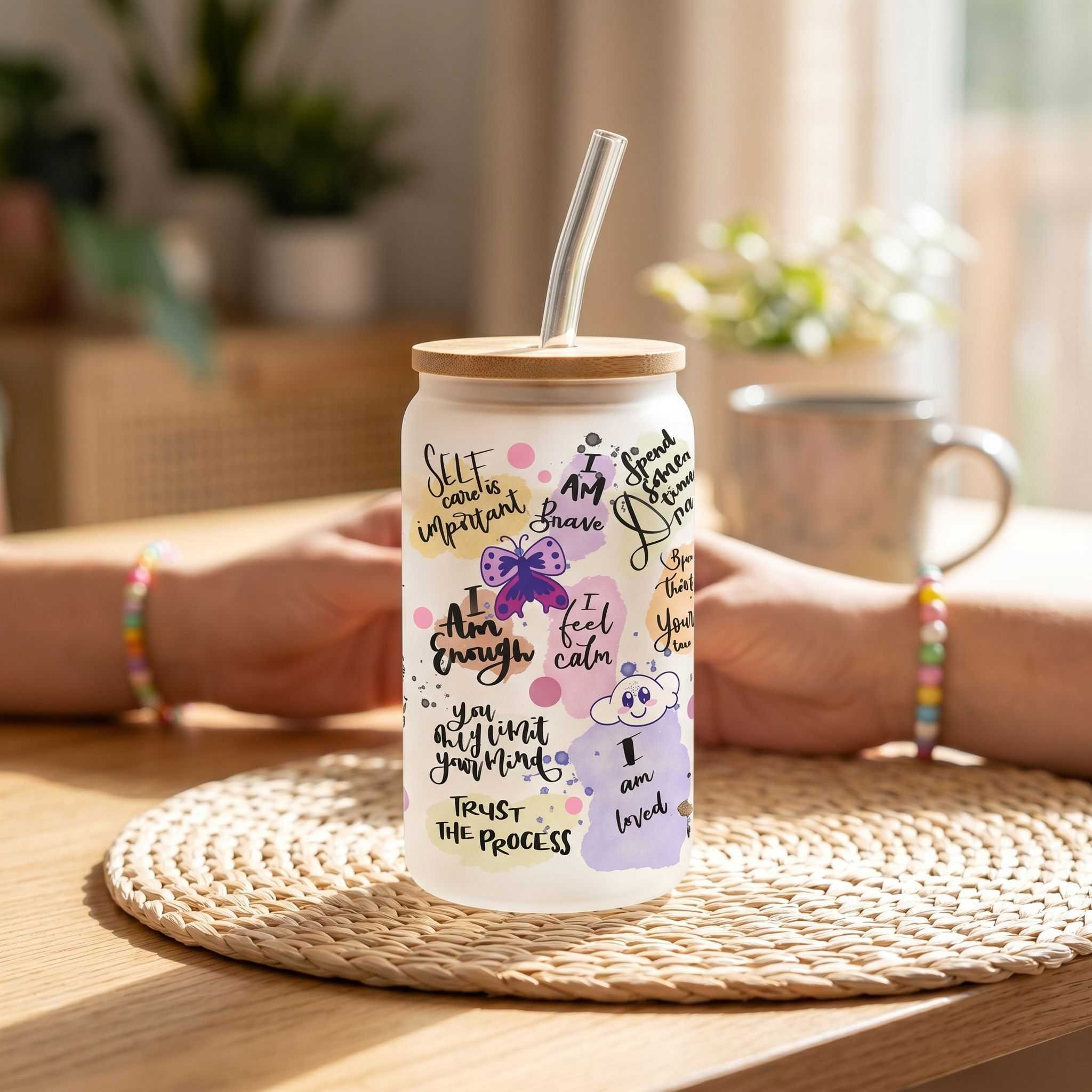 Close-up of a clear glass Libby beer can style cup with positive affirmations, set against a textured rustic surface with sunlight reflections.