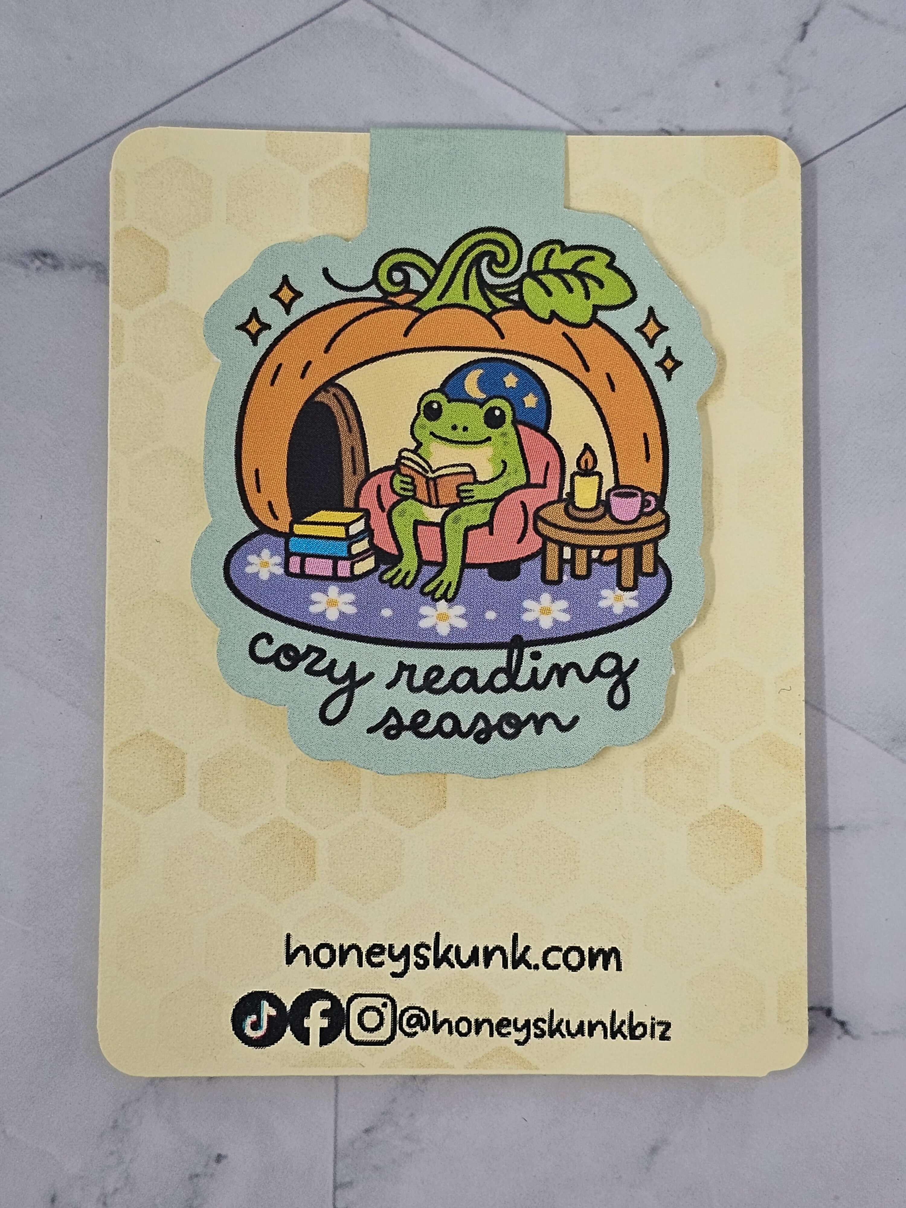 Frog magnetic bookmark featuring a frog in a pumpkin house, promoting cozy reading season.