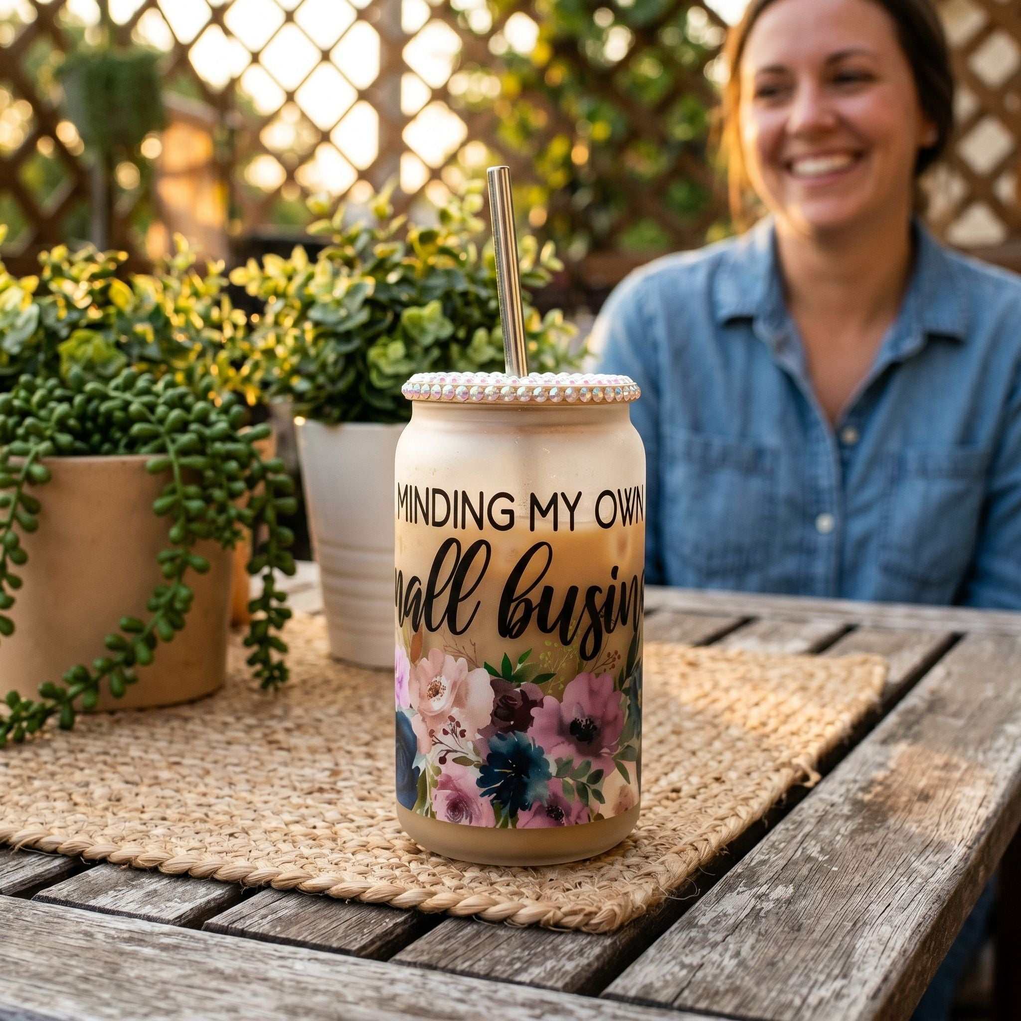 Frosted floral Libby beer can tumbler on outdoor patio table, warm sunlight, greenery, cheerful casual setting.